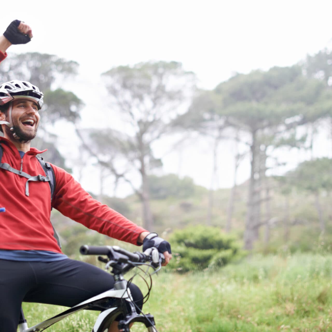 A young male athlete pumping his fist in the air after conquering a mountain biking trail