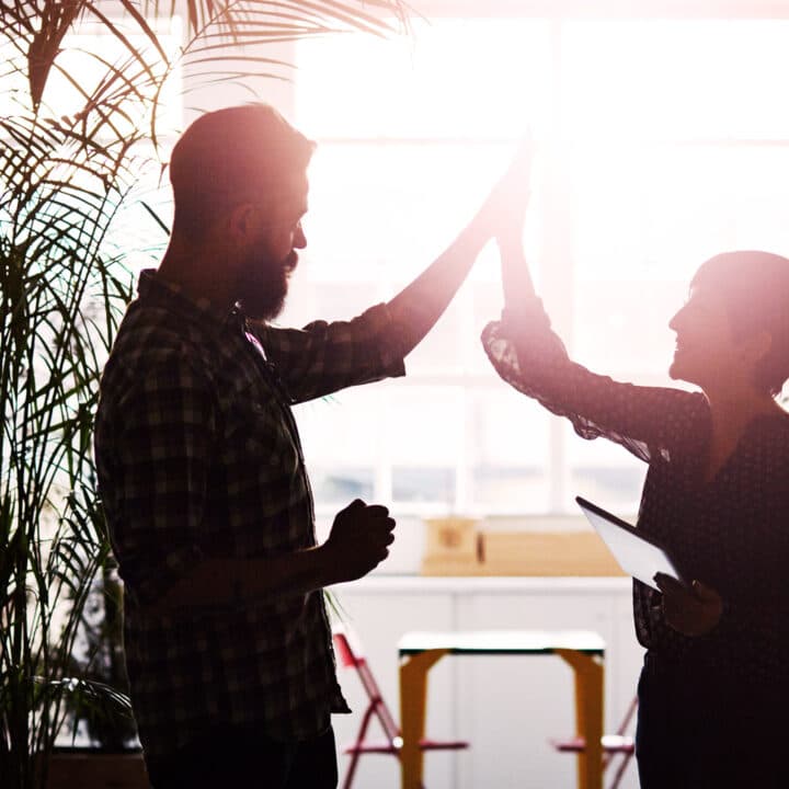 Två kolleger gör high-five på ett kontor.