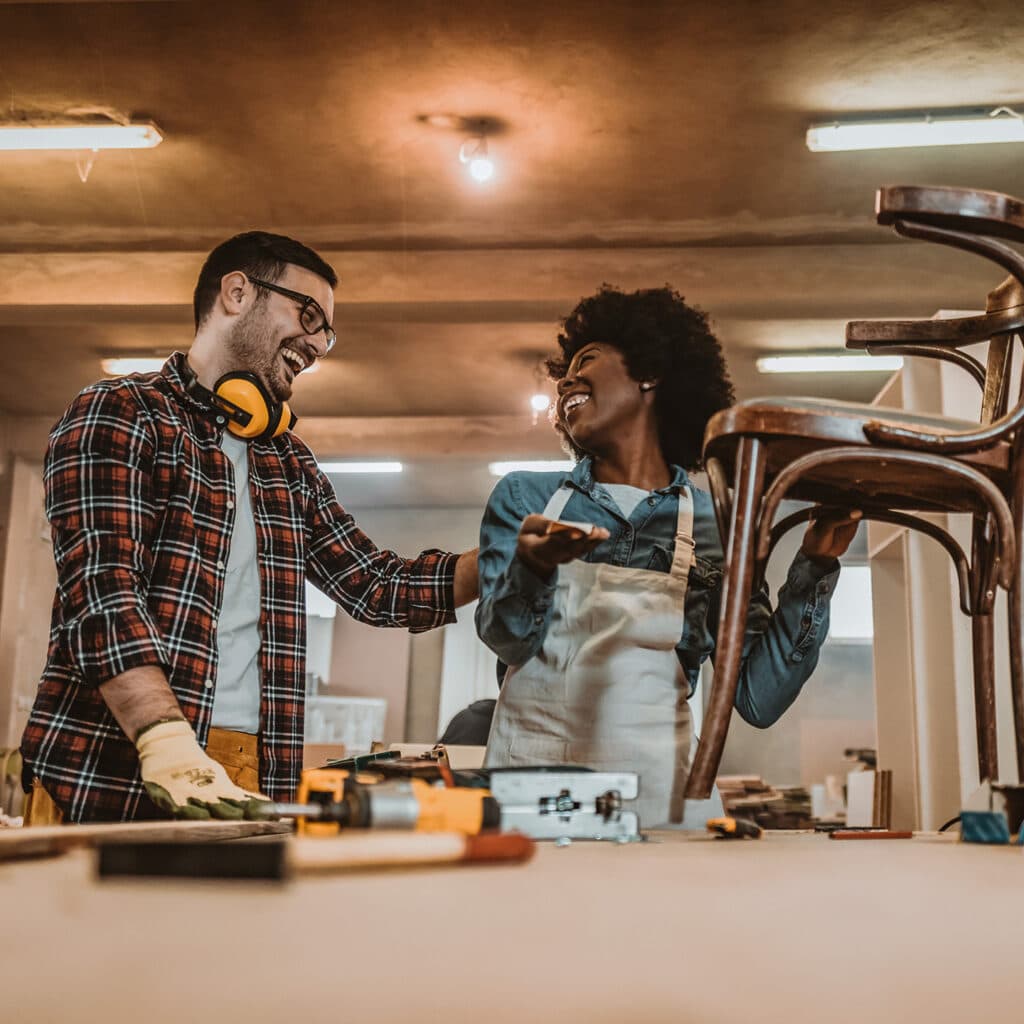 Till miljöpolicysidorna. One African-American Woman and African-American man carpenters using tools for restoration wooden chair in studio