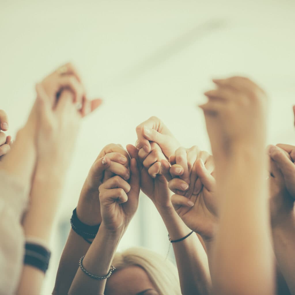 Group of women standing toghether in the circle and holding raised hands. Close up of hands. Unrecognizable people.